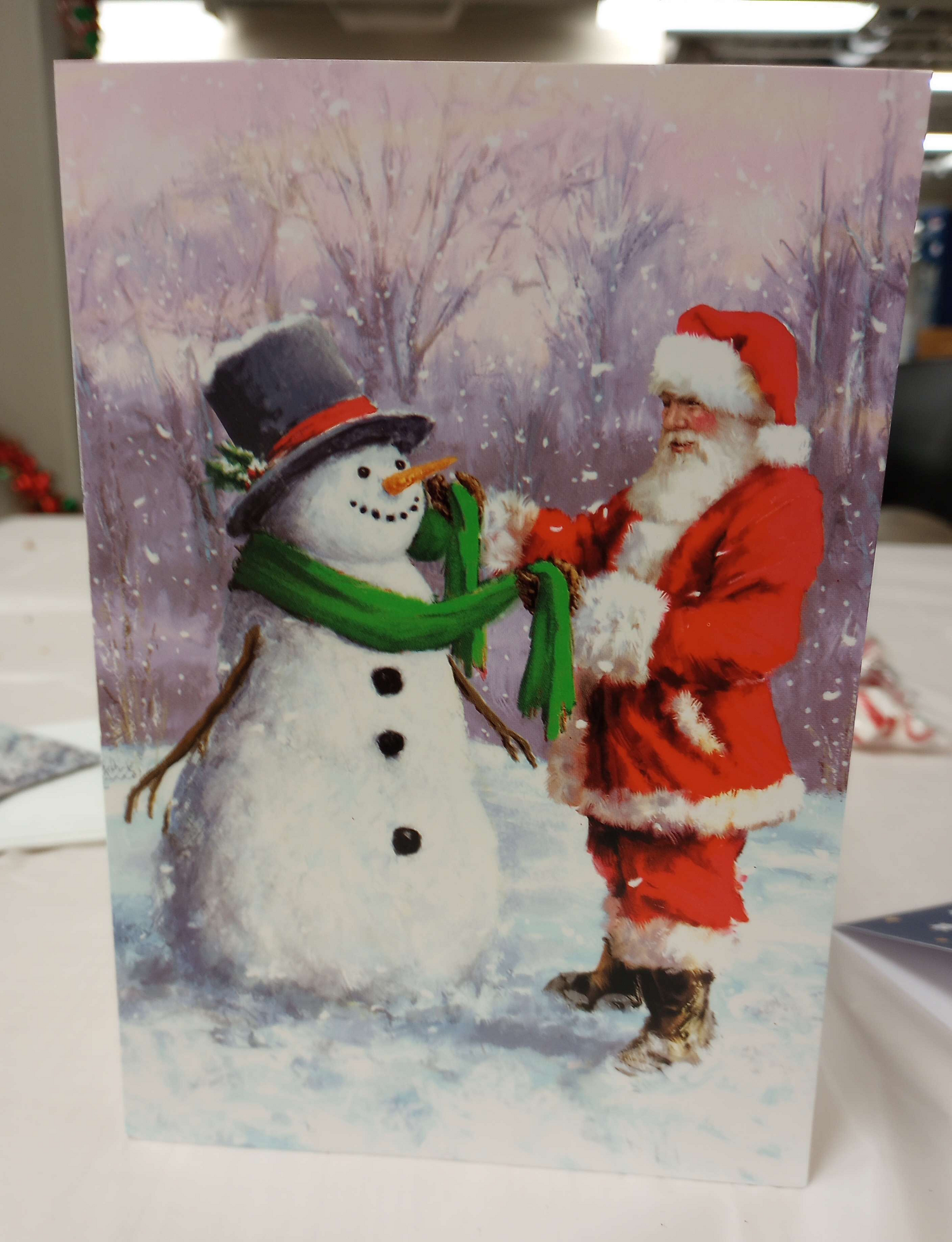 A rather svelte Santa is seen wrapping a scarf around a snowman.